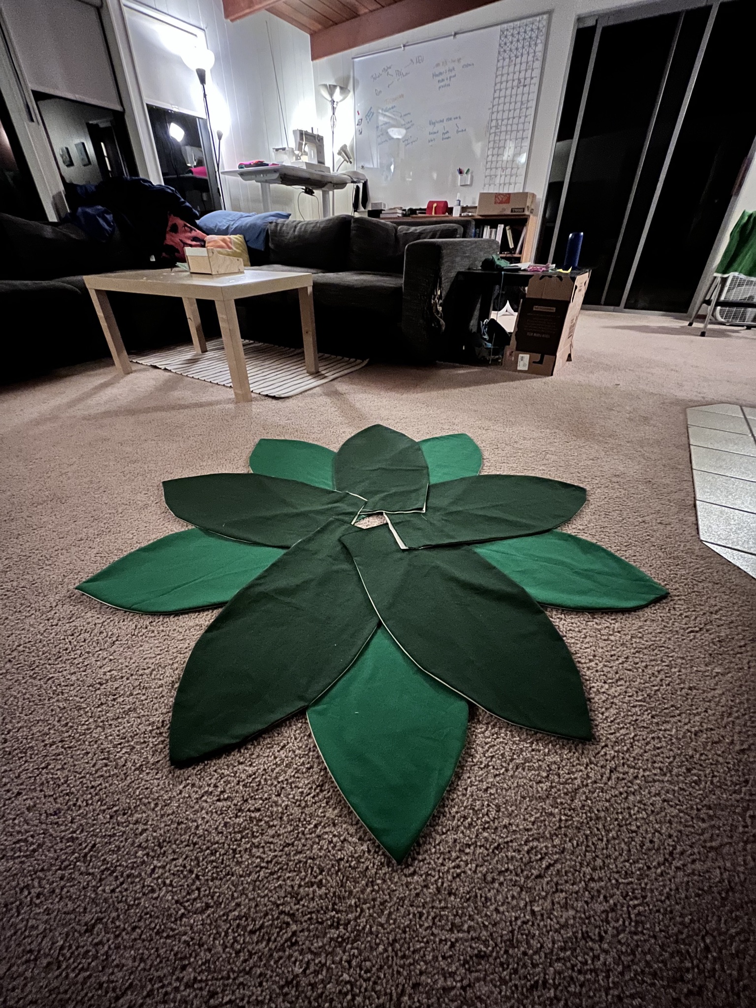 Dark and lighter green leaf fabric shapes laid out in a circle on a carpeted floor in a dim living room