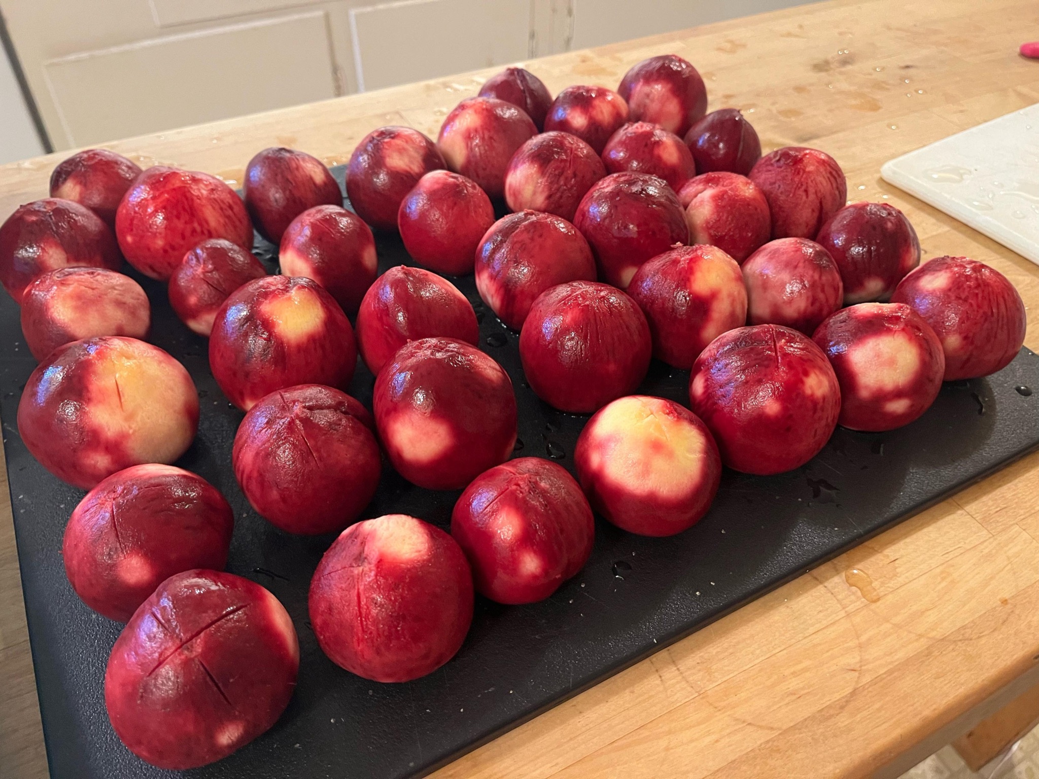 Shiny wet peeled peaches in red and some yellow lined up 5x7 on a black cutting board