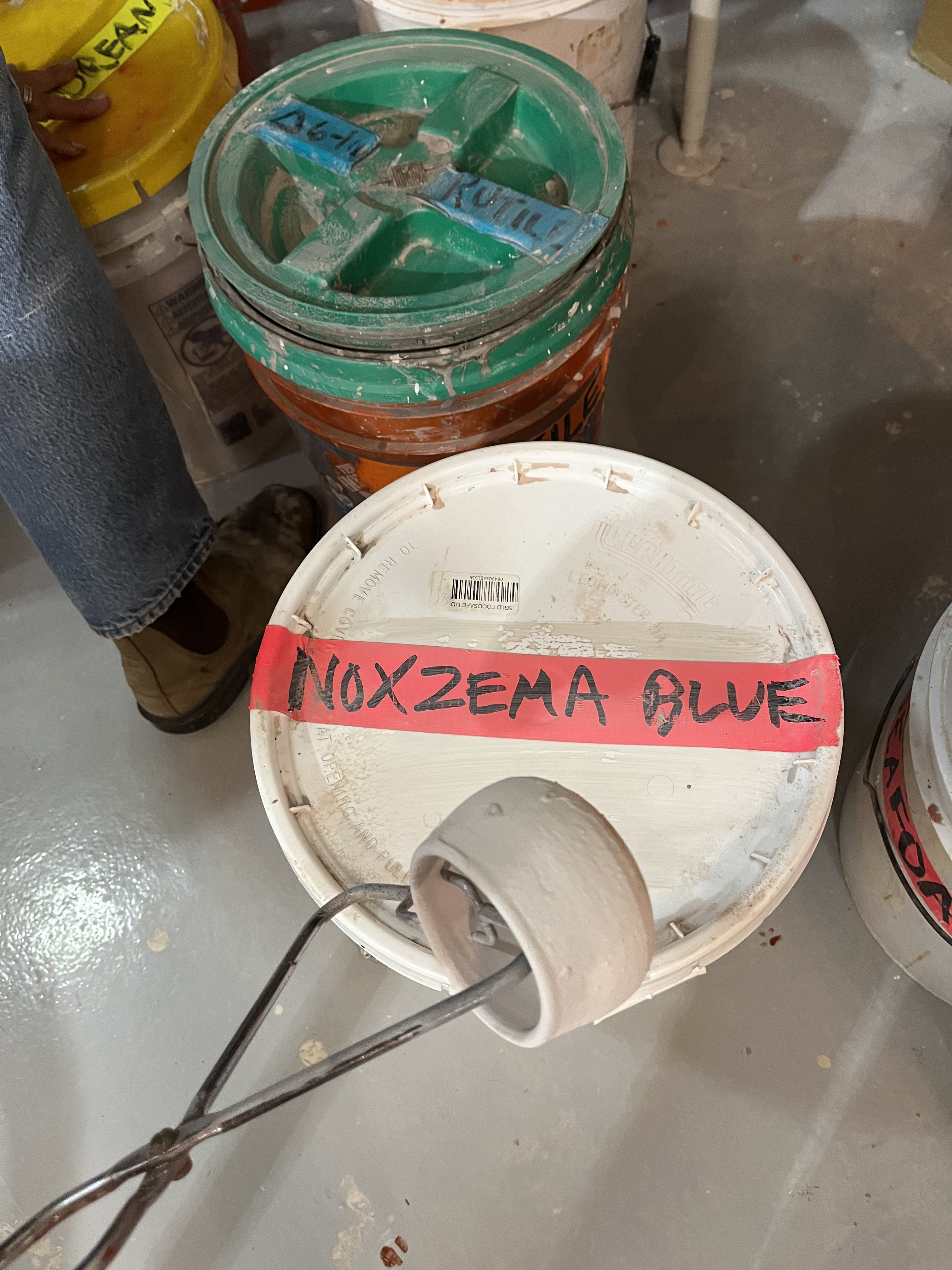 Holding a pot above a bucket of glaze labeled Noxema Blue.