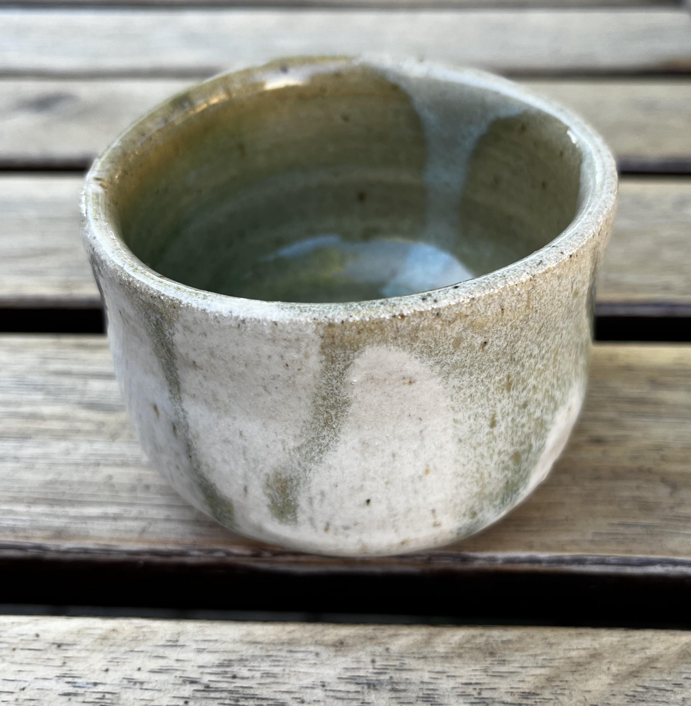 A mug/pot with green and white drips of glaze that almost seem inverted on the inside vs the outside.