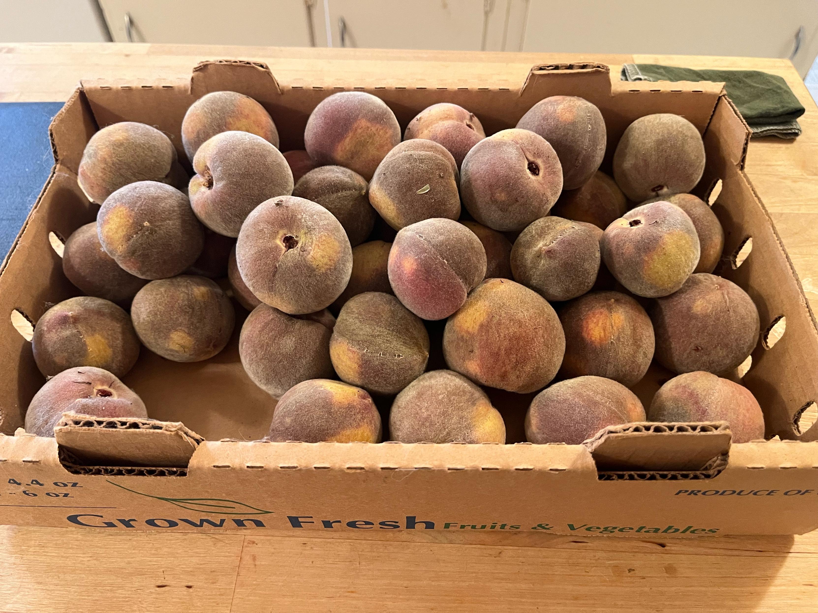 Produce box of a pile of about 30 dark peaches