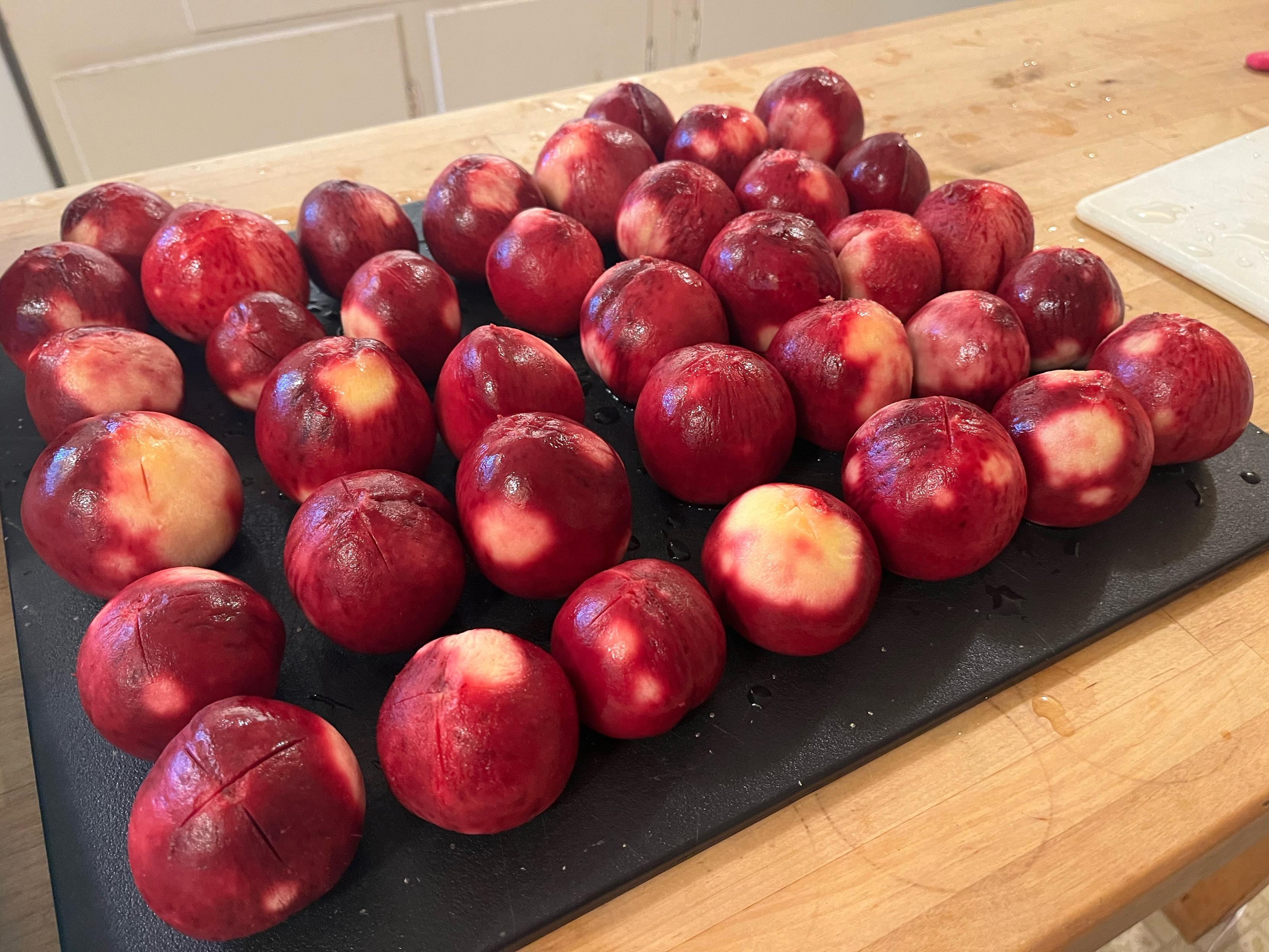 Shiny wet peeled peaches in red and some yellow lined up 5x7 on a black cutting board